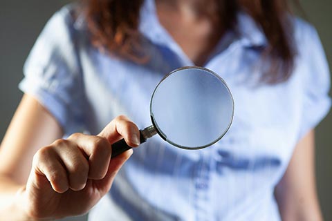 Woman holding a magnifying glass, representing careful assessment and earlier cancer detection.