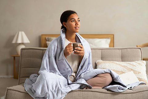 Woman wrapped in a blanket with tea, reflecting tiredness after winter and considering a spring blood check